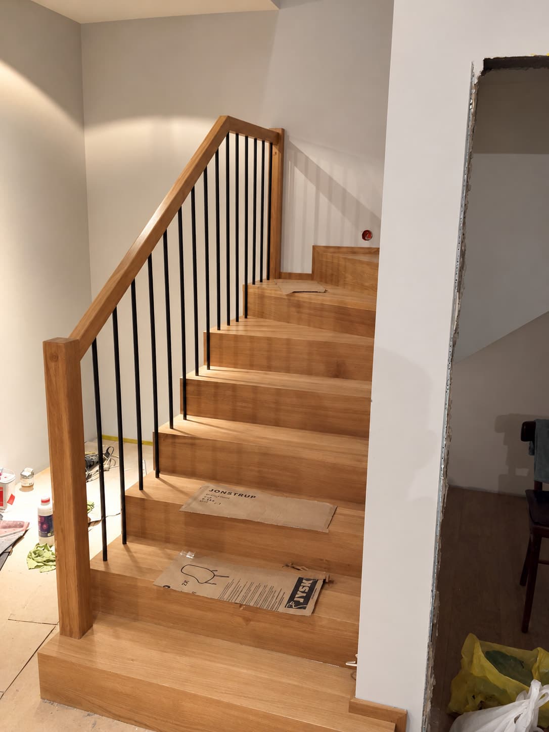 Proste drewniane schody z czarną, pionową balustradą.