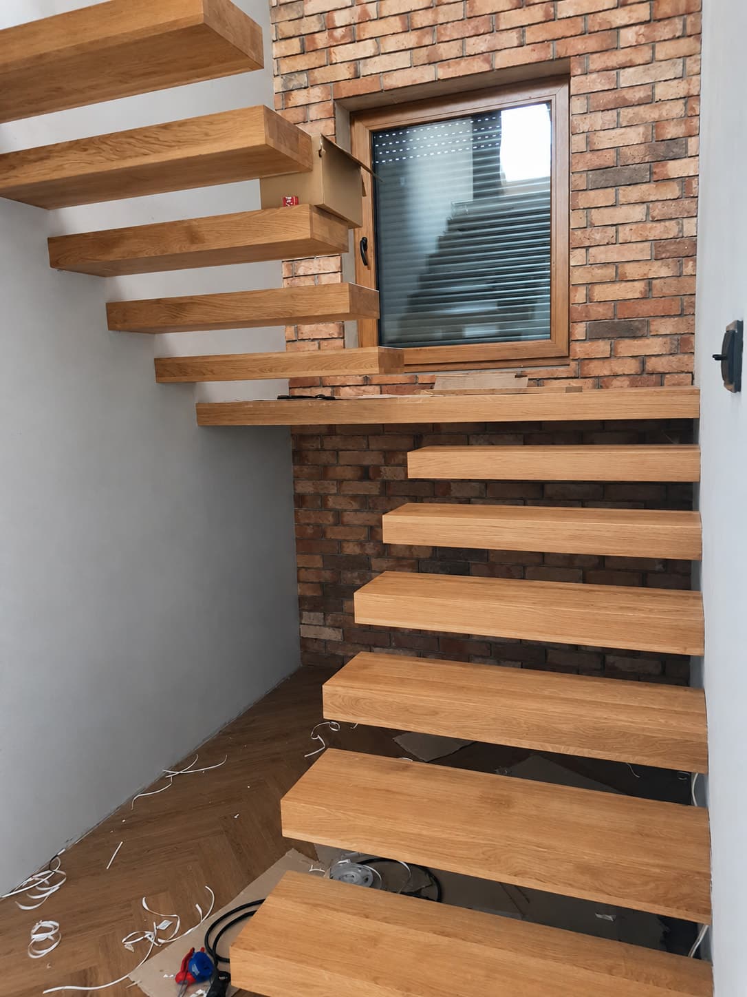 Drewniane stopnie z ciemnymi mocowaniami na ceglanej ścianie.