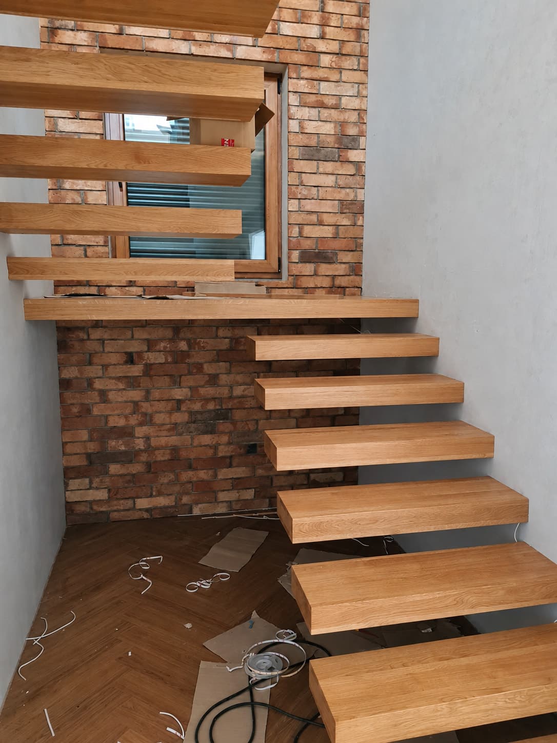 Wiszące drewniane stopnie z czarnymi wspornikami na ceglanej ścianie.