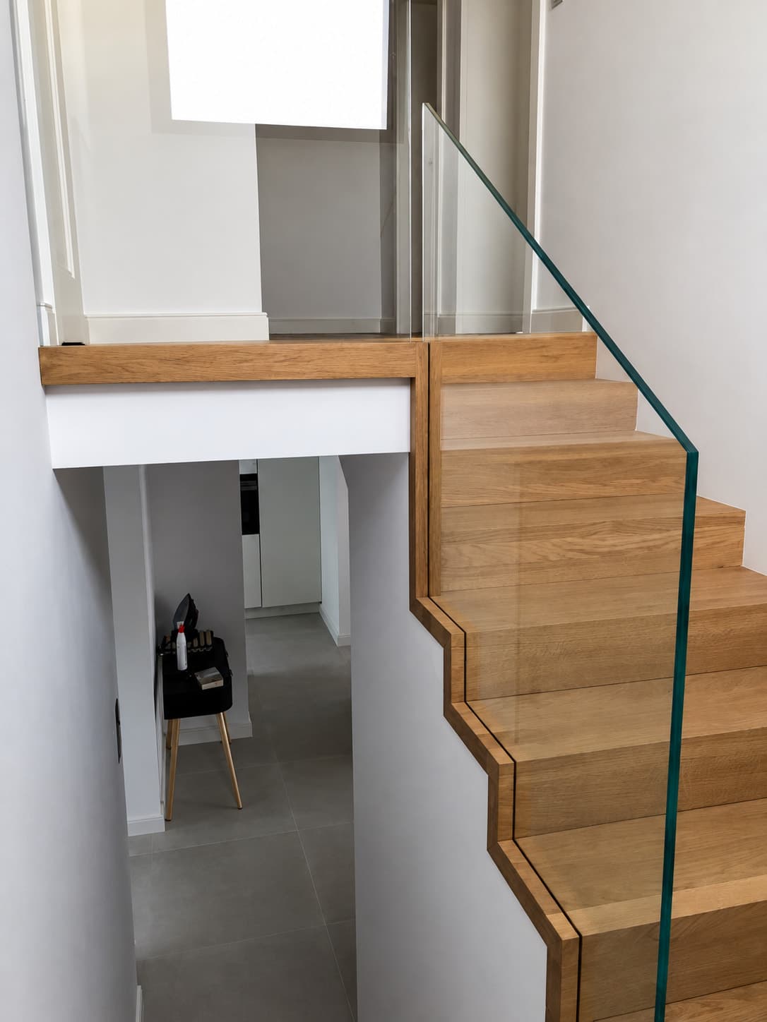 Drewniane schody z przezroczystą szklaną balustradą.